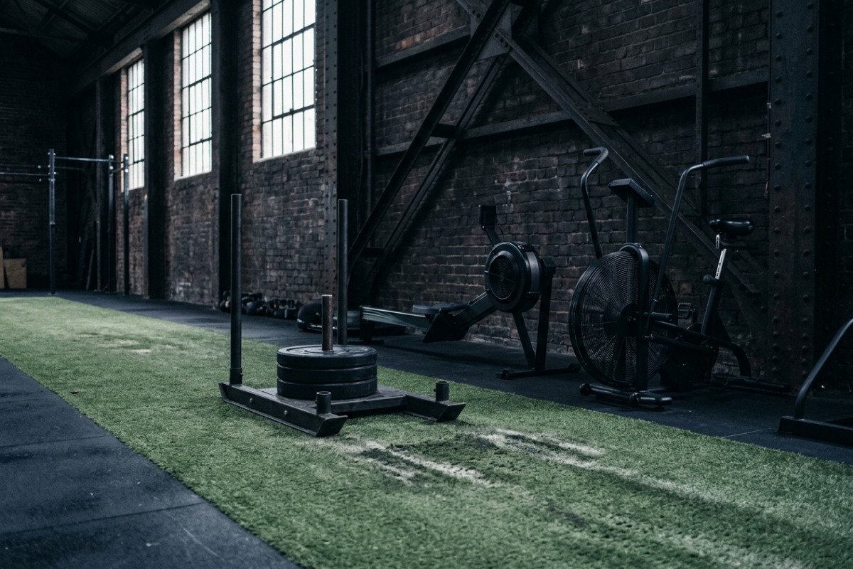 A weighted push sled on the turf lane, with a rower and an air bike lined up along the depot wall