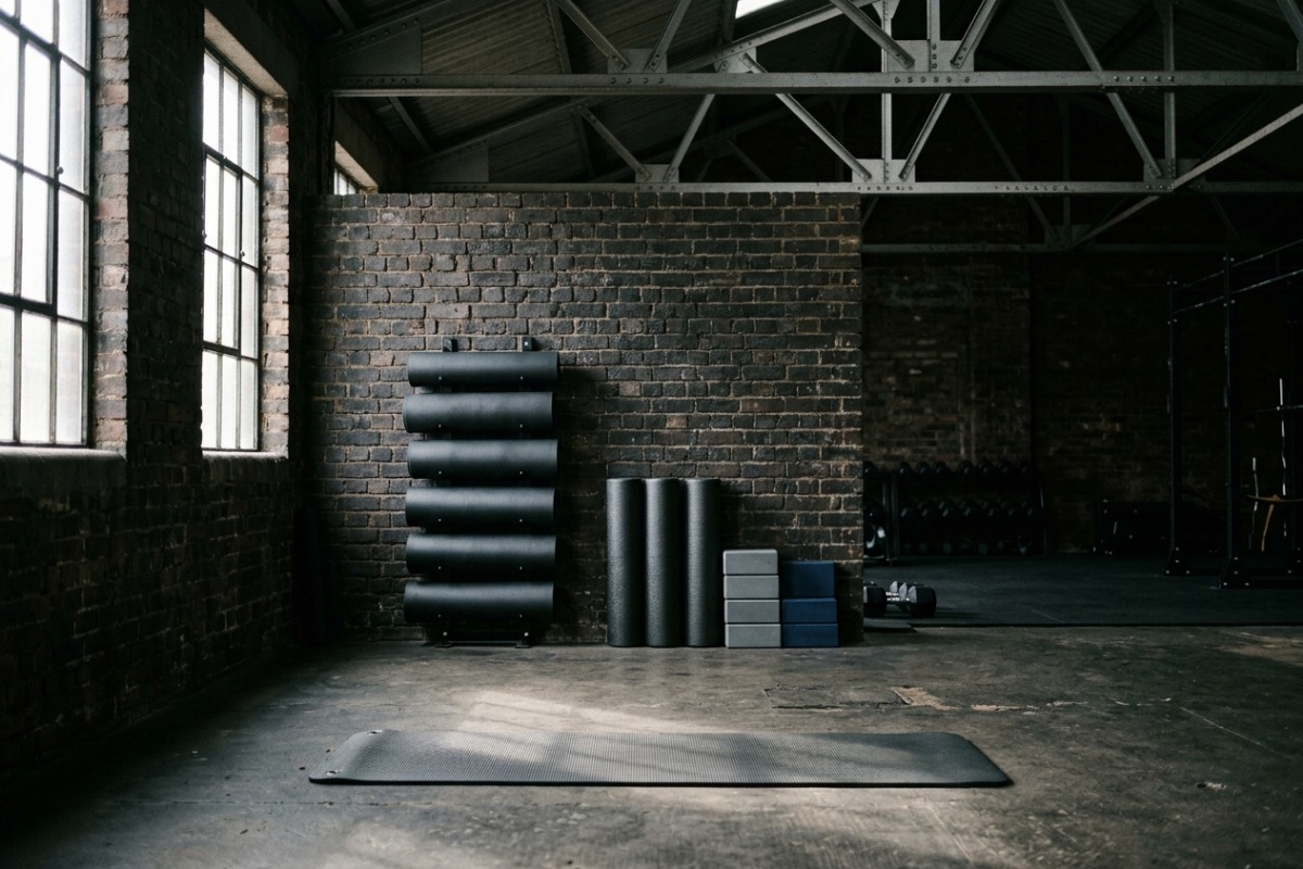 Rolled mats on a wall rack beside foam rollers and blocks, one mat unrolled on the floor
